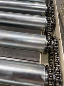 Detalle del sistema de transmisión por cadena de un transportador de rodillos motorizado por bucle de cadena para paneles de armario de gran peso.